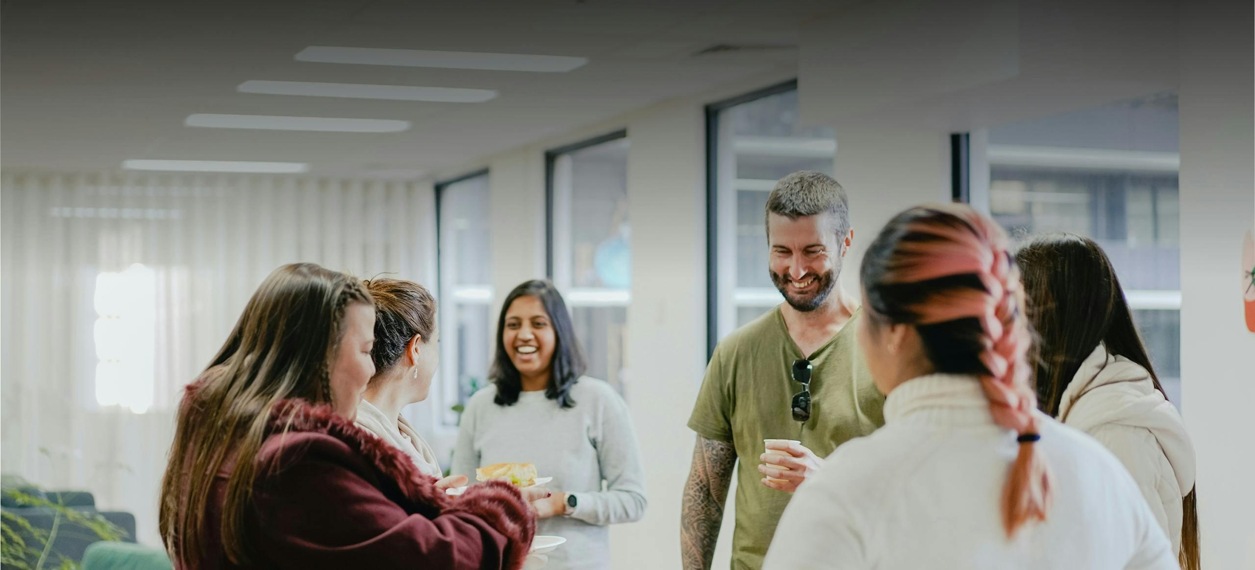 A group of office coworkers stood up, enjoying a hot beverage together