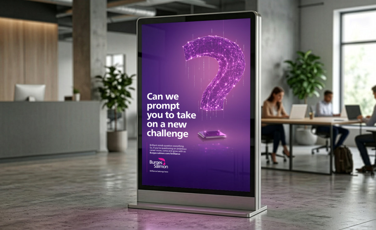Digital billboard in an office with a glowing purple question mark and a prompt about taking on new challenges. Workers in the background are using laptops.