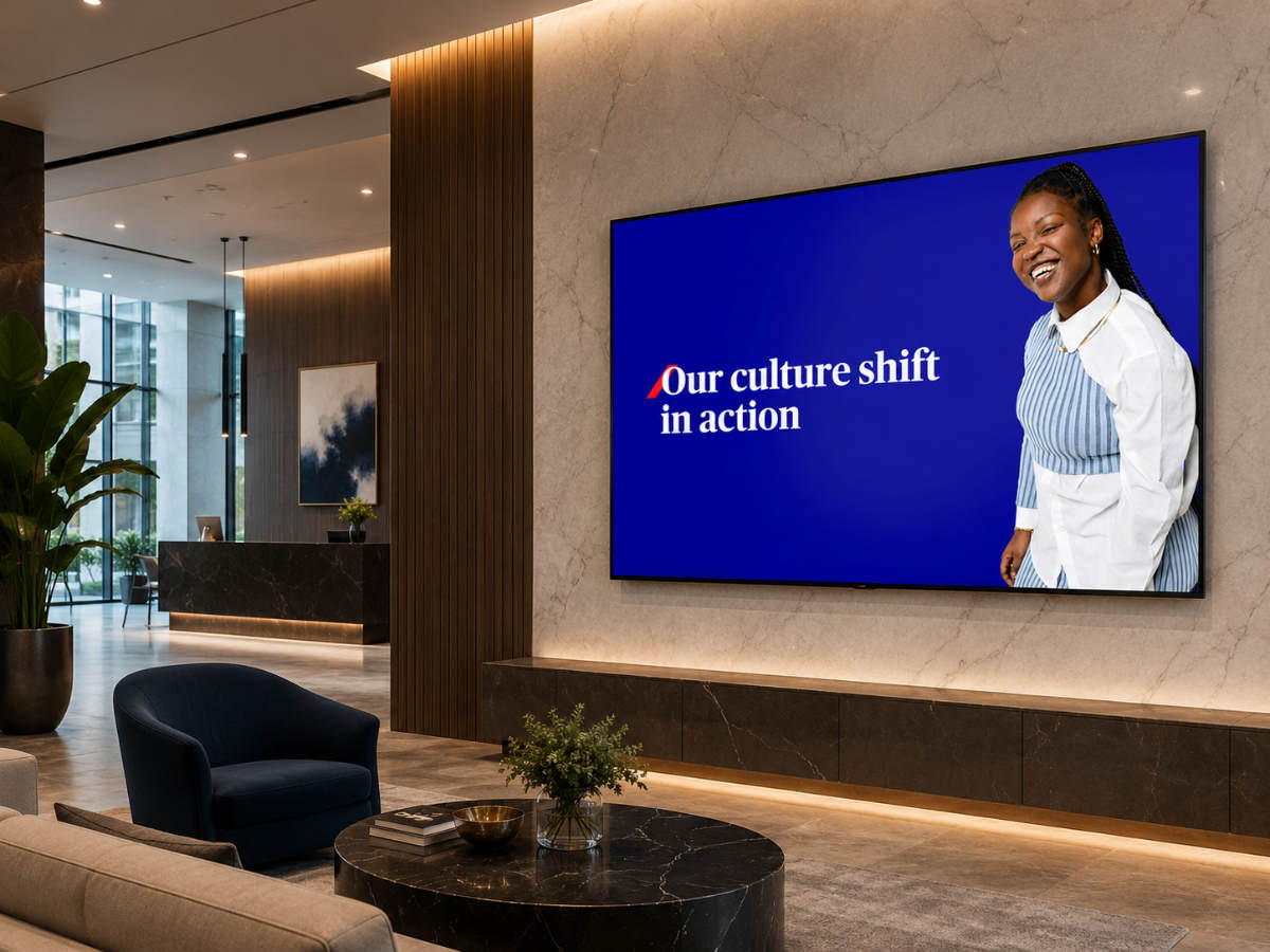 Modern lobby with sleek decor and a large screen displaying “Our culture shift in action” beside a smiling woman, conveying positivity and change.
