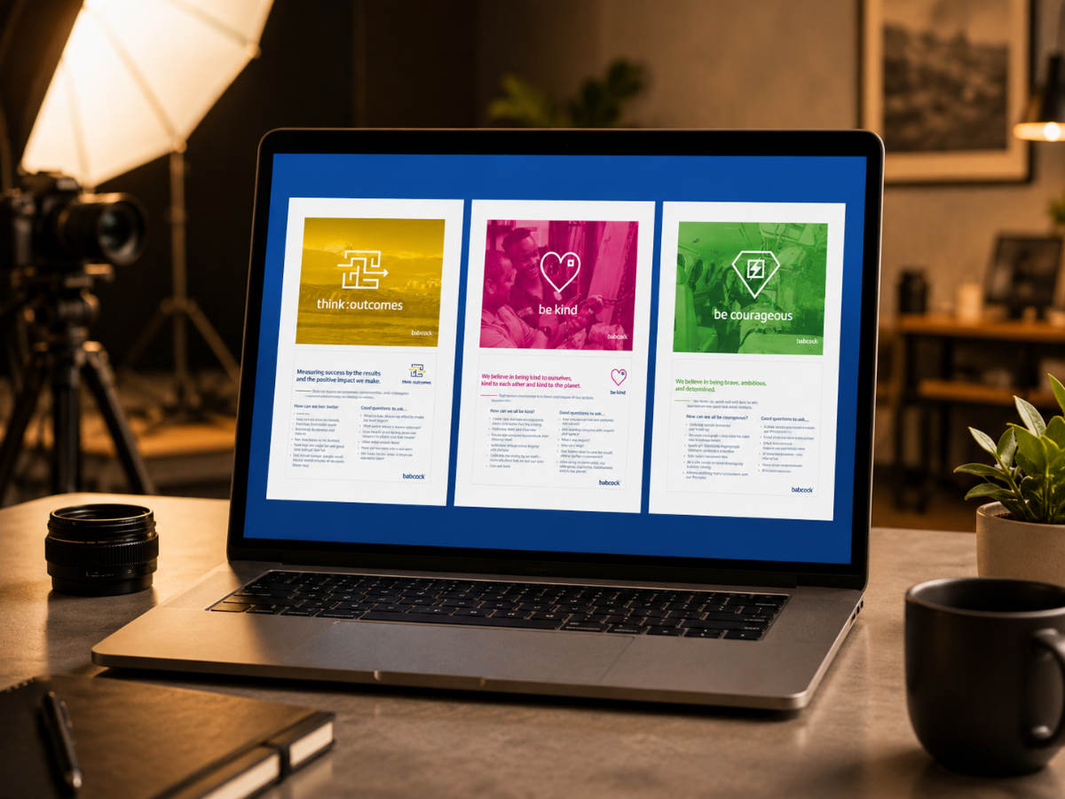 A laptop on a desk displays three posters: yellow